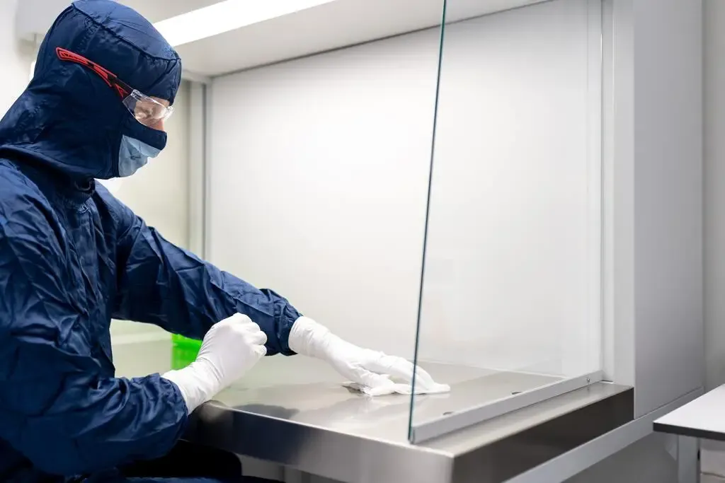 Technicien en tenue de protection désinfectant un plan de travail en inox
